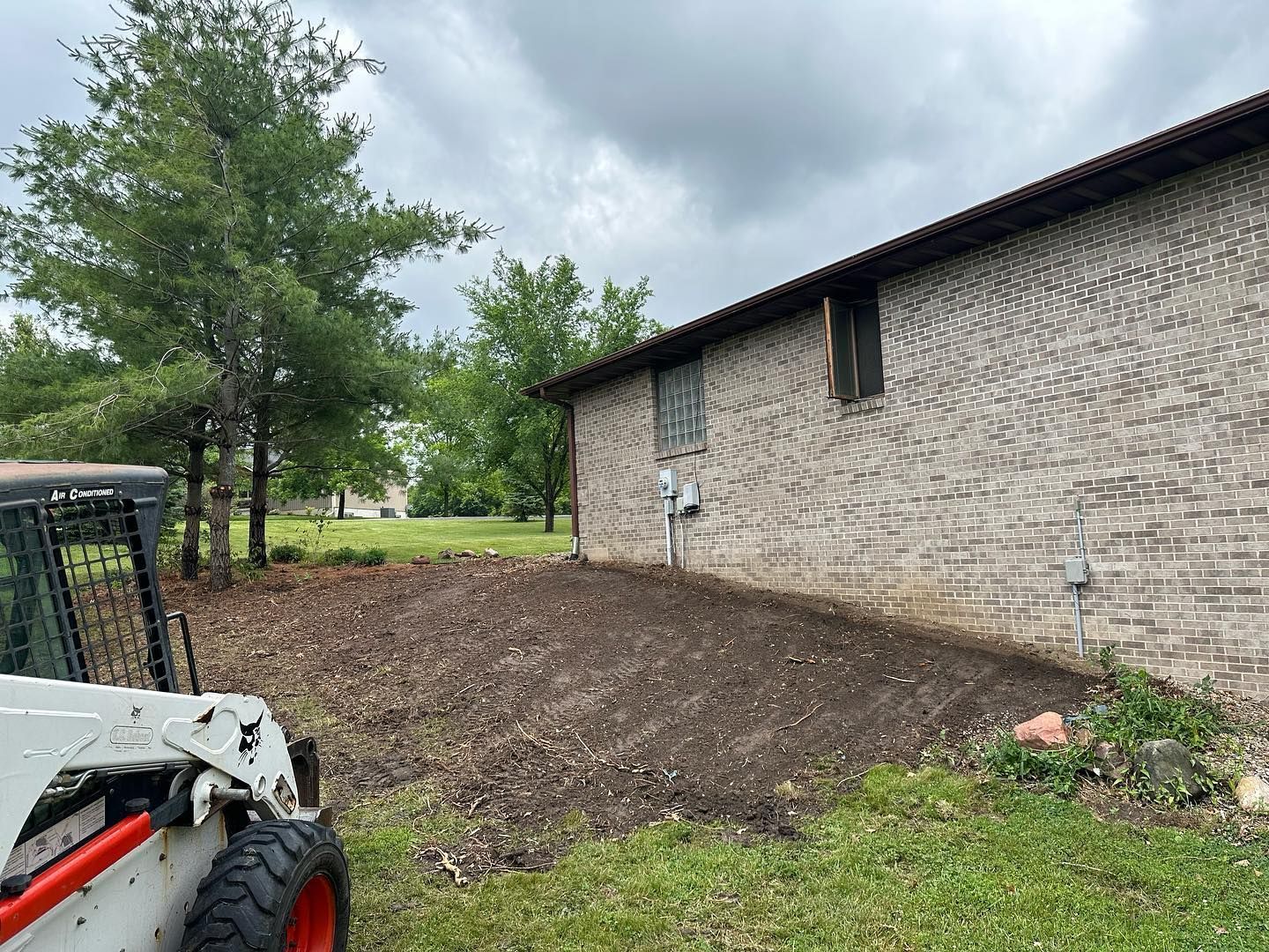 A small skid steer in a yard next to a brick building, ground covered with mulch.