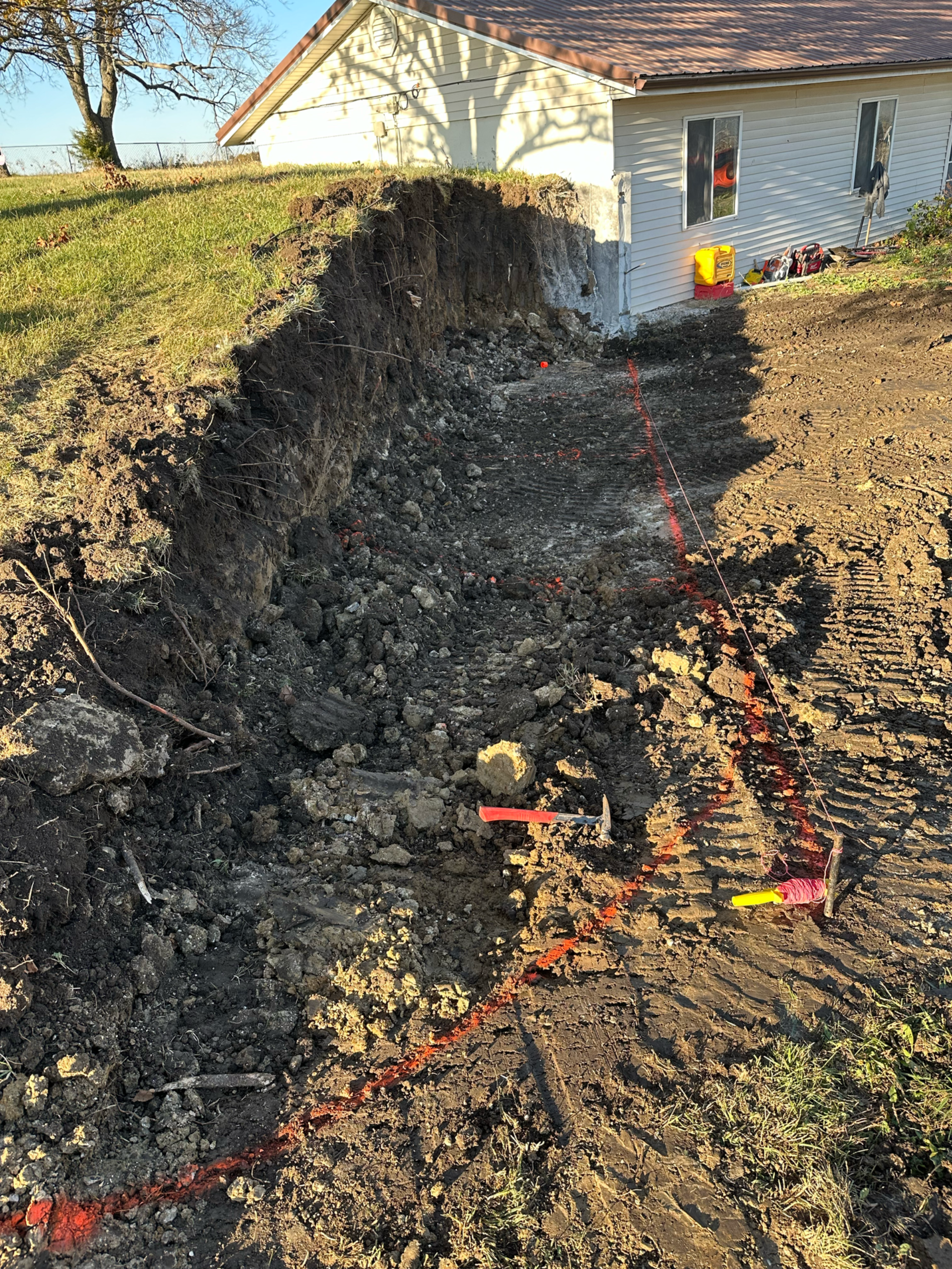 A deep trench dug alongside a house, exposing soil and indicating construction.