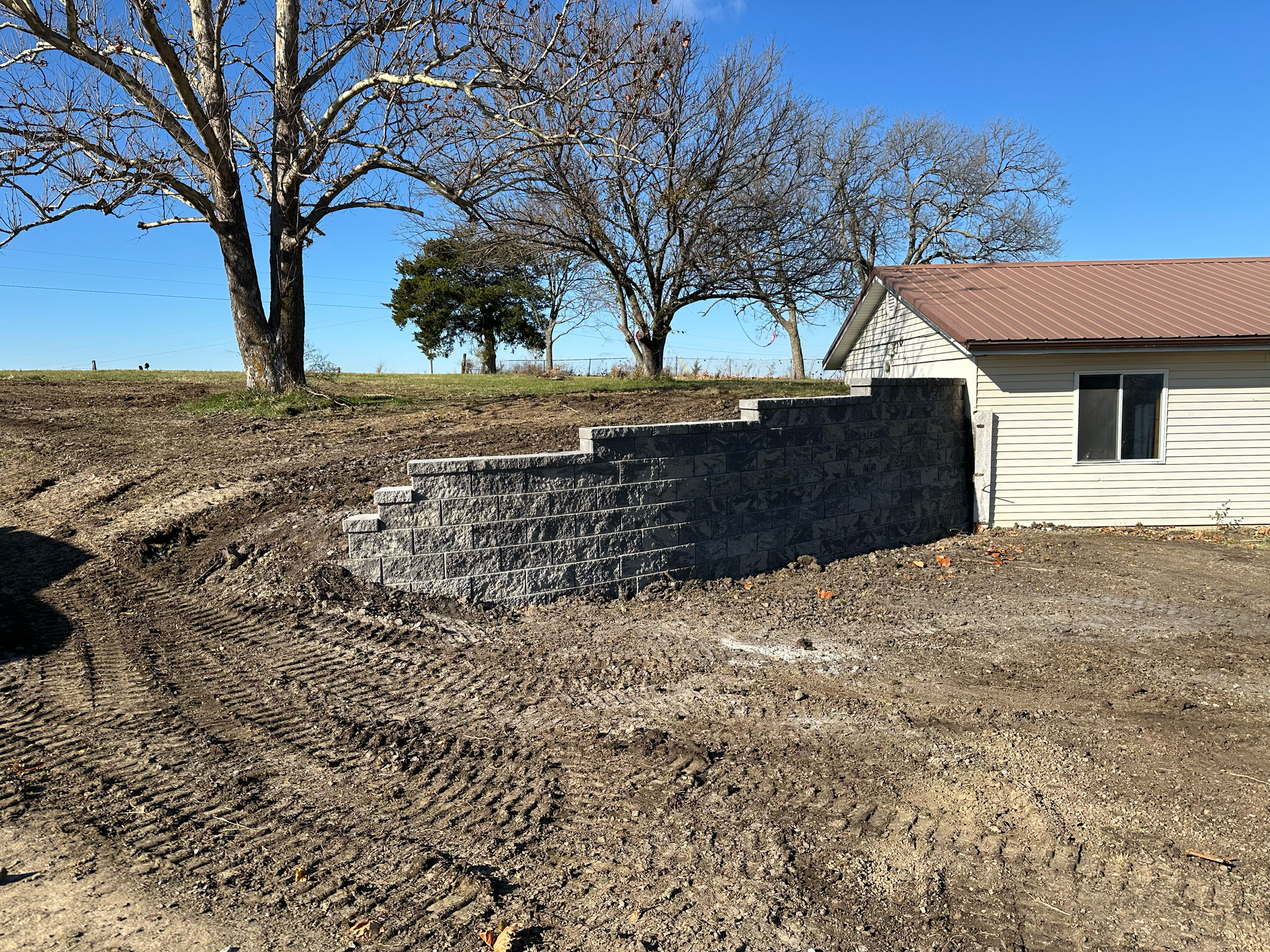 Stone retaining wall with steps next to a building and trees in a field.