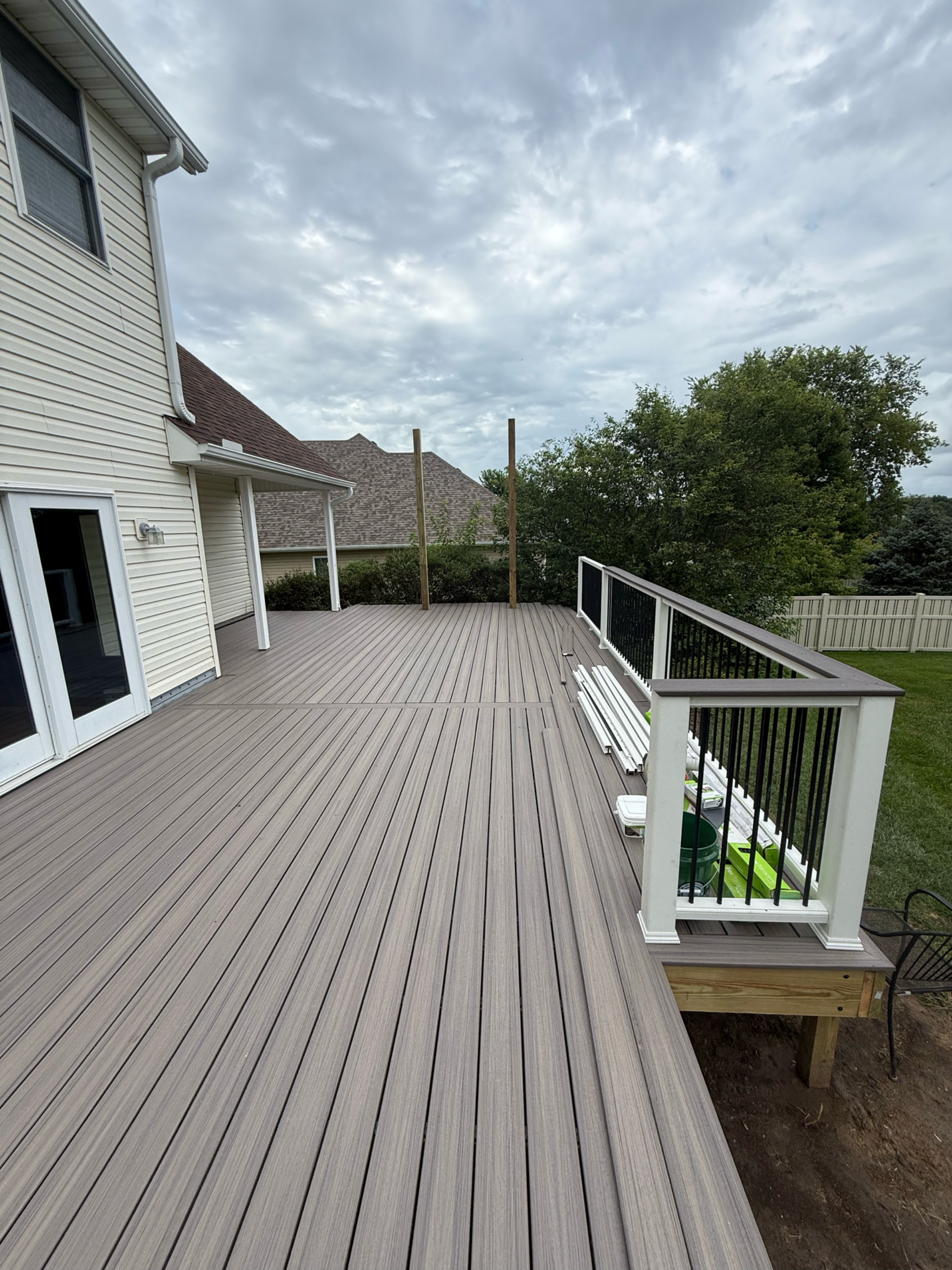Large grey composite deck with black railing, attached to a white house, cloudy sky.