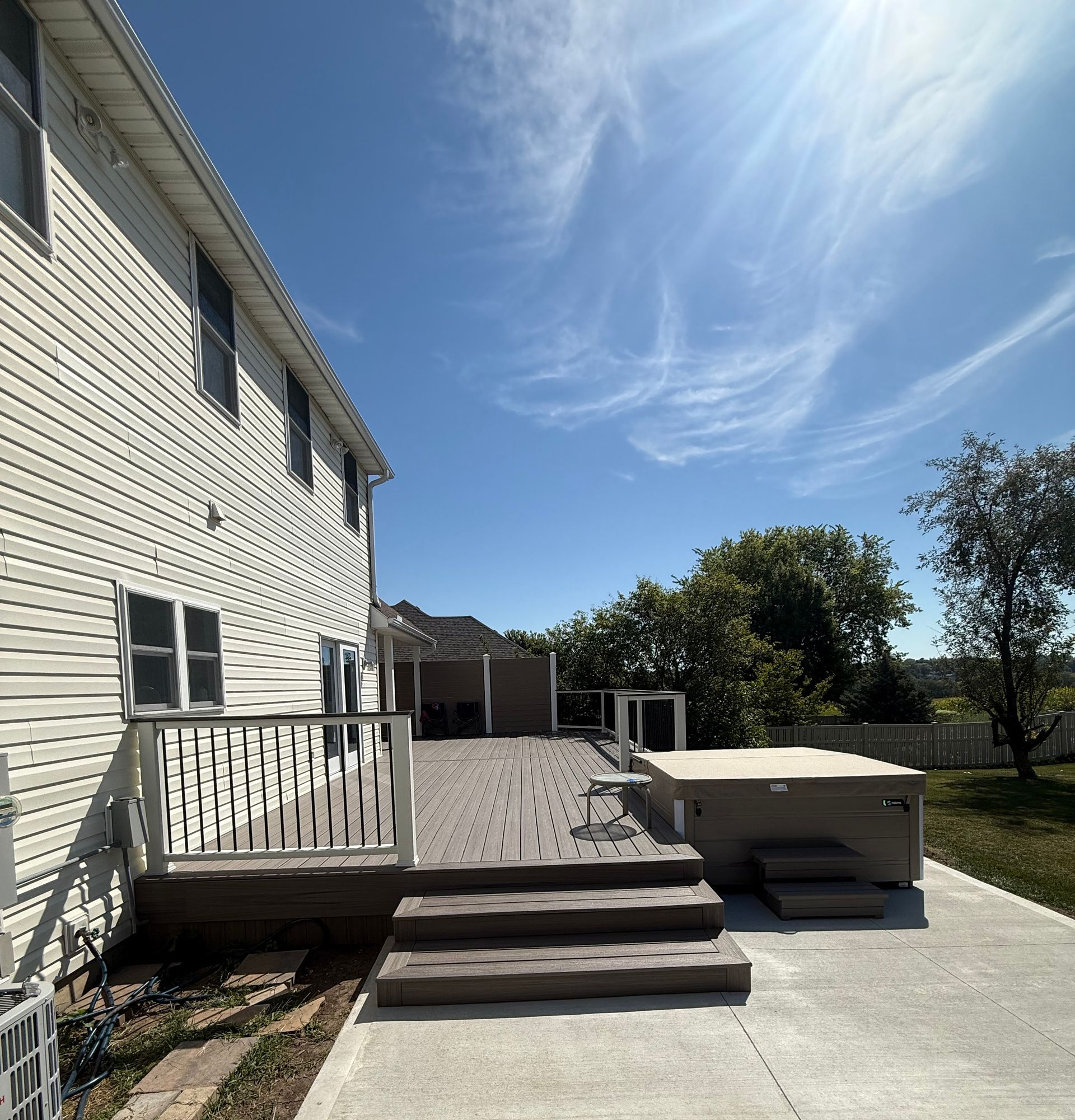 Side of a house with a deck and hot tub on a sunny day.