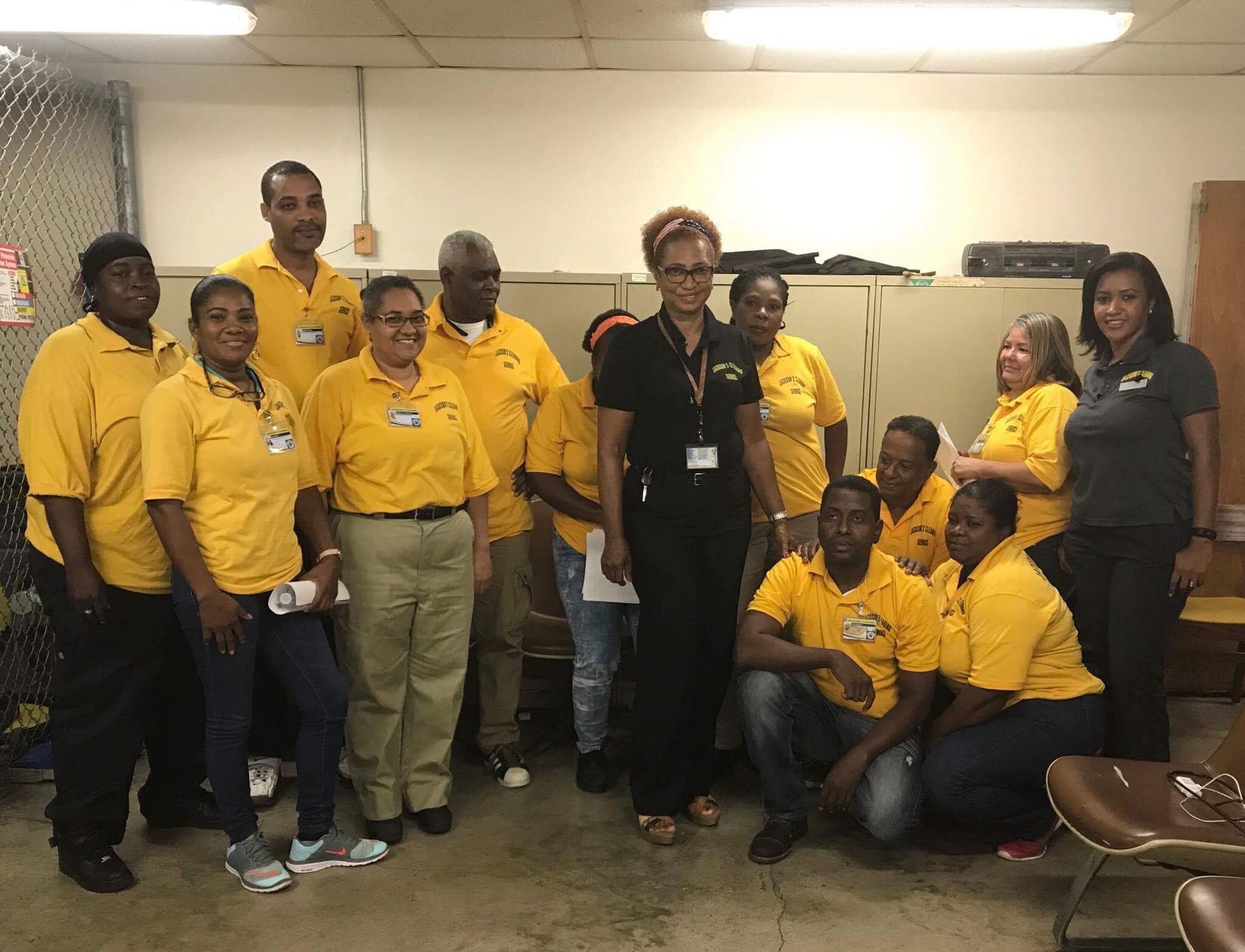 Group of people in yellow shirts, some kneeling, in a room. Some are wearing name tags.