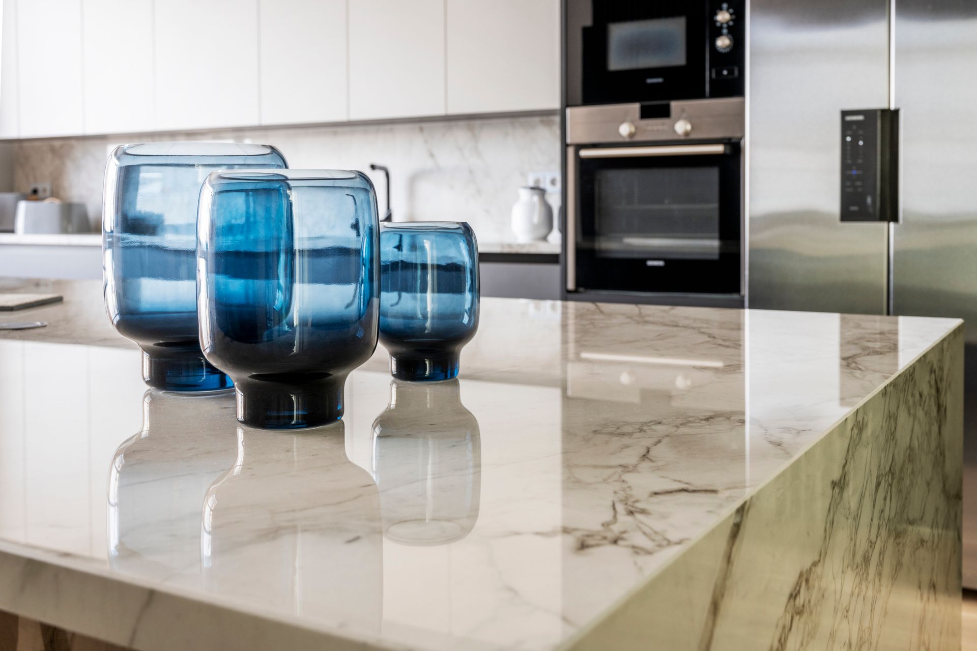 Marble island detail of a large kitchen with stainless steel appliances and blue glass vases. Marble island detail of a large kitchen with stainless steel appliances and blue glass vases.