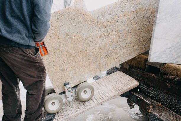 A construction worker bringing a granite countertop down from a truck.