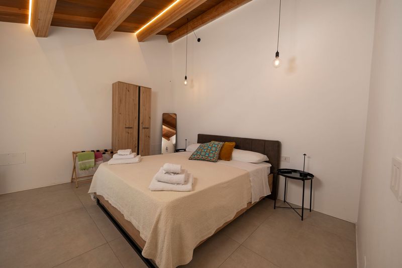 Camera da letto minimalista con letto in legno, lenzuola bianche e un'ampia finestra sopra la testiera.