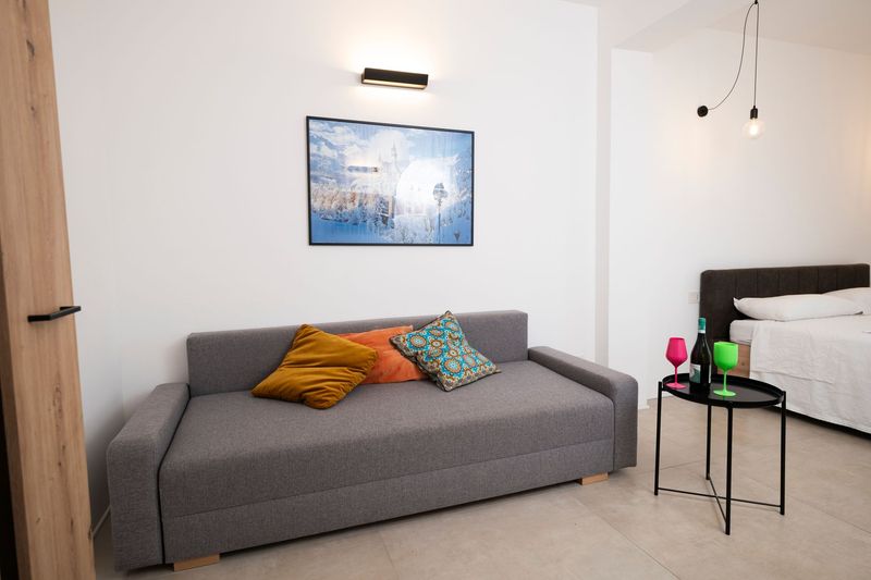 Camera da letto minimalista con divano grigio, letto matrimoniale e valigia sul pavimento.