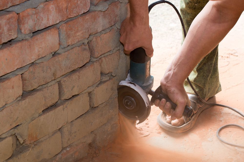 Person Uses an Angle Grinder on A Brick Wall, Creating Dust — Ultra Services Ground Pavement & Building in Cowra, NSW