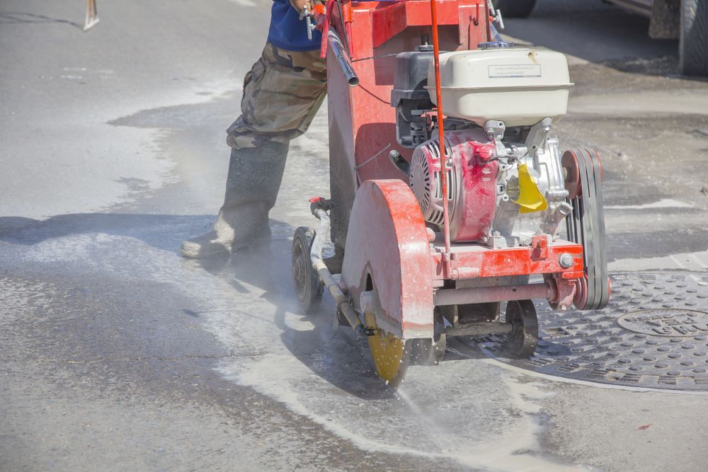 Worker Using a Red Concrete Saw to Cut a Roadway, Creating Dust — Ultra Services Ground Pavement & Building in Bourke, NSW