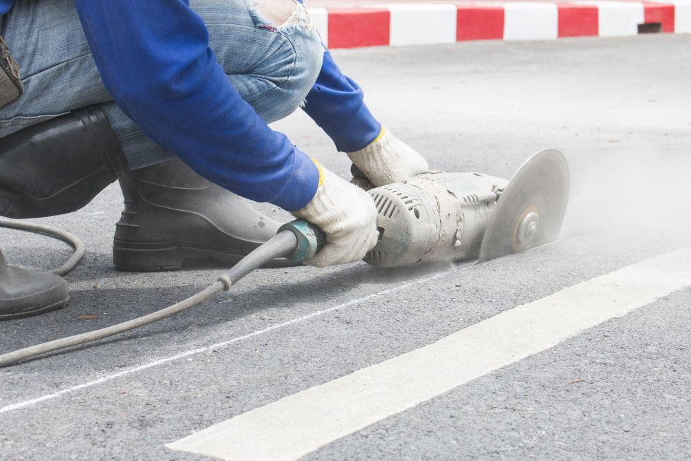 Person Cutting a White Line on Asphalt with A Power Saw — Ultra Services Ground Pavement & Building in Abercrombie, NSW