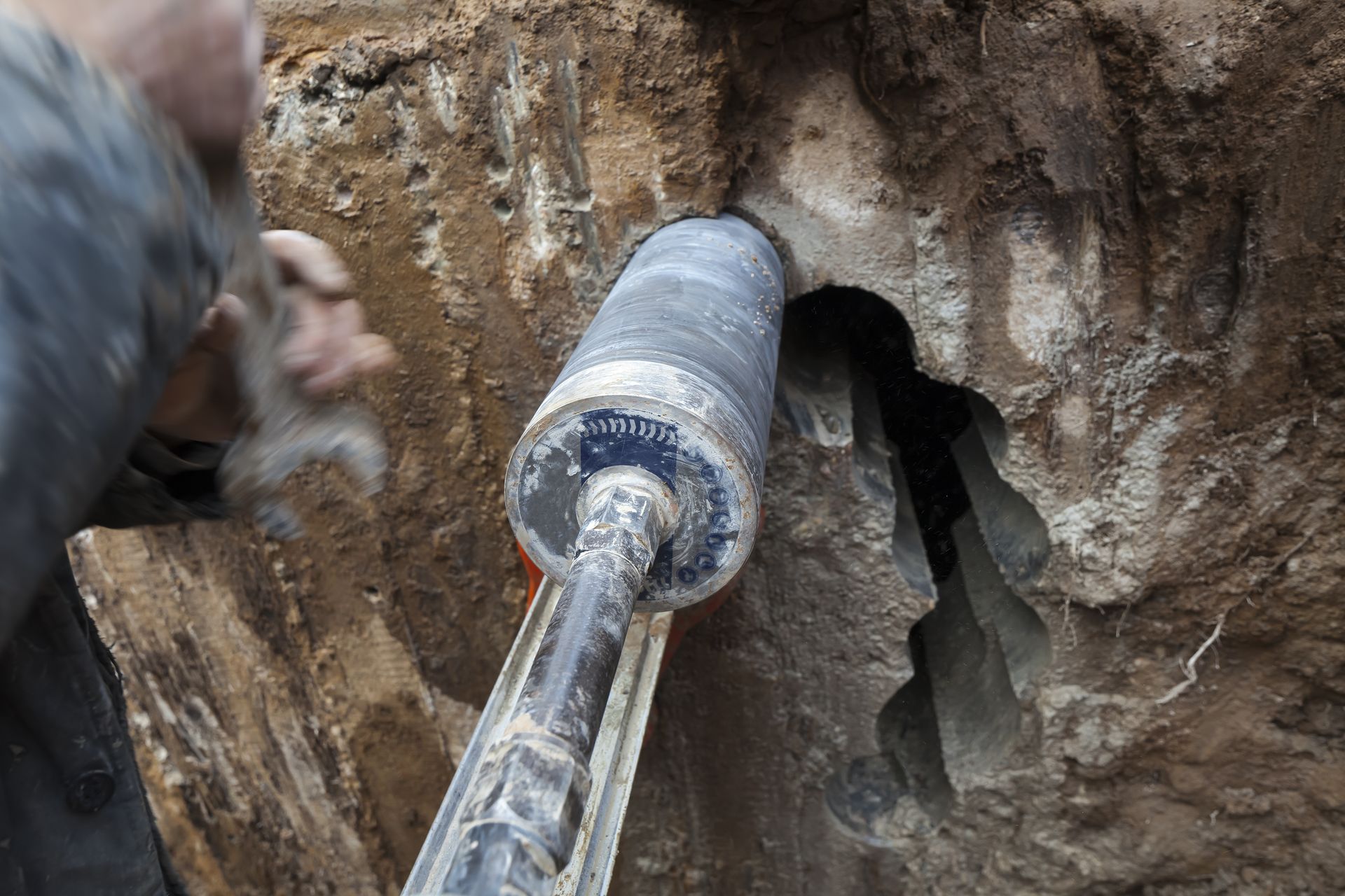Person Drilling a Large Hole in A Dirt Wall with A Power Drill — Ultra Services Ground Pavement & Building in Cowra, NSW