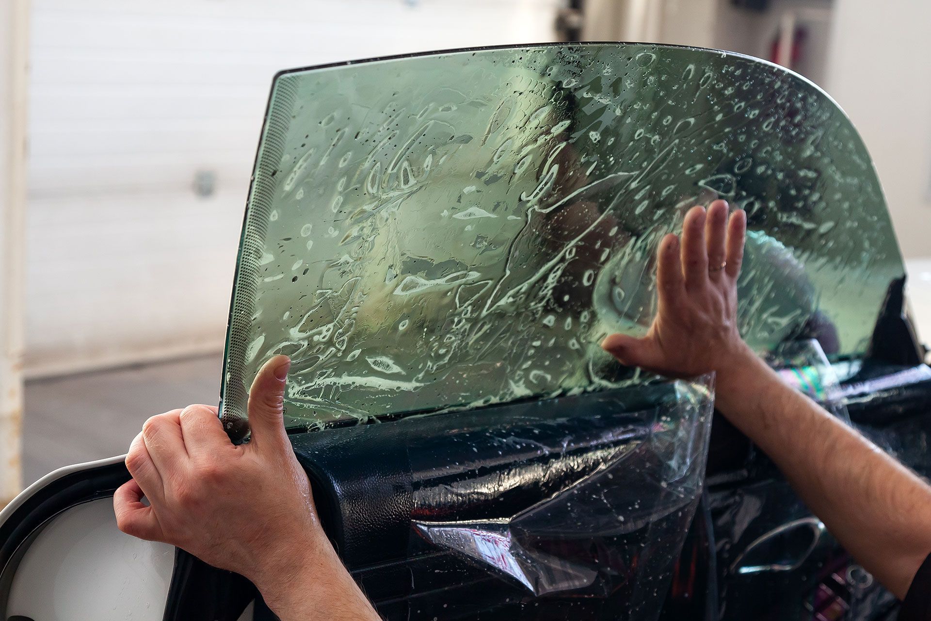 The wizard for installing additional equipment sticks a tint film on the side front glass of the car and flattens it by hand to fit the glass with a greenish tint in the auto service