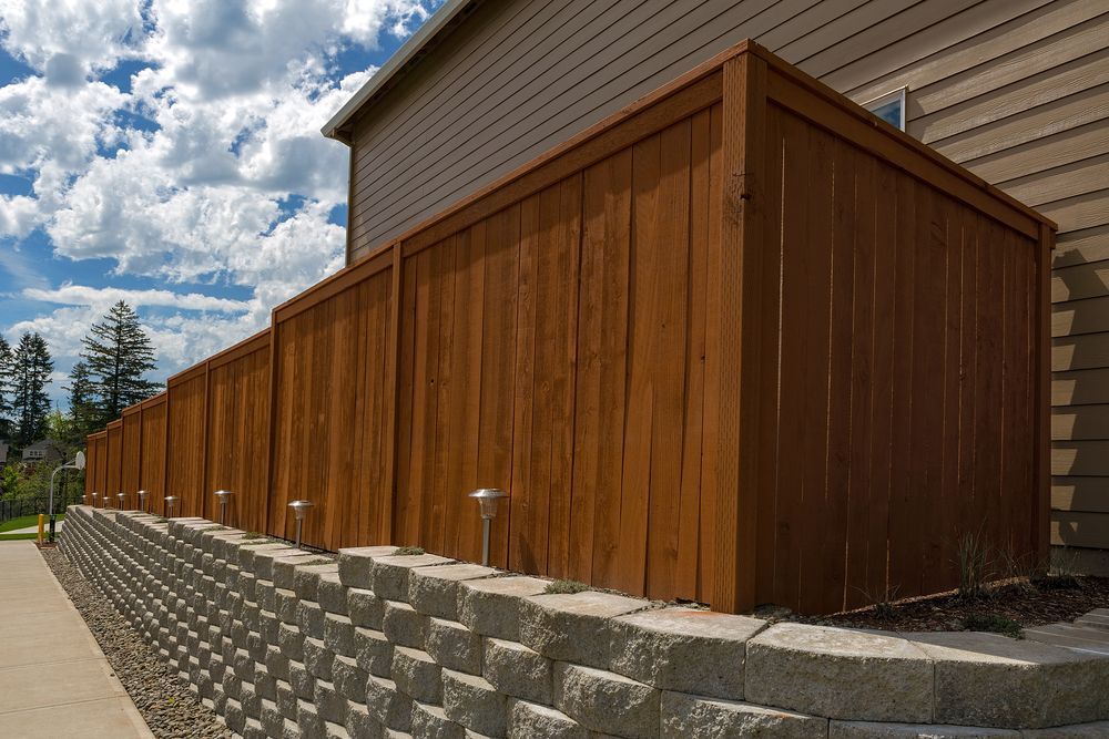 A wooden fence surrounds a stone wall next to a house.