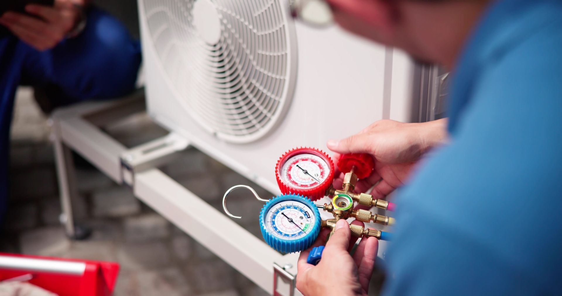 HVAC technician using gauges to service an outdoor air conditioning unit.