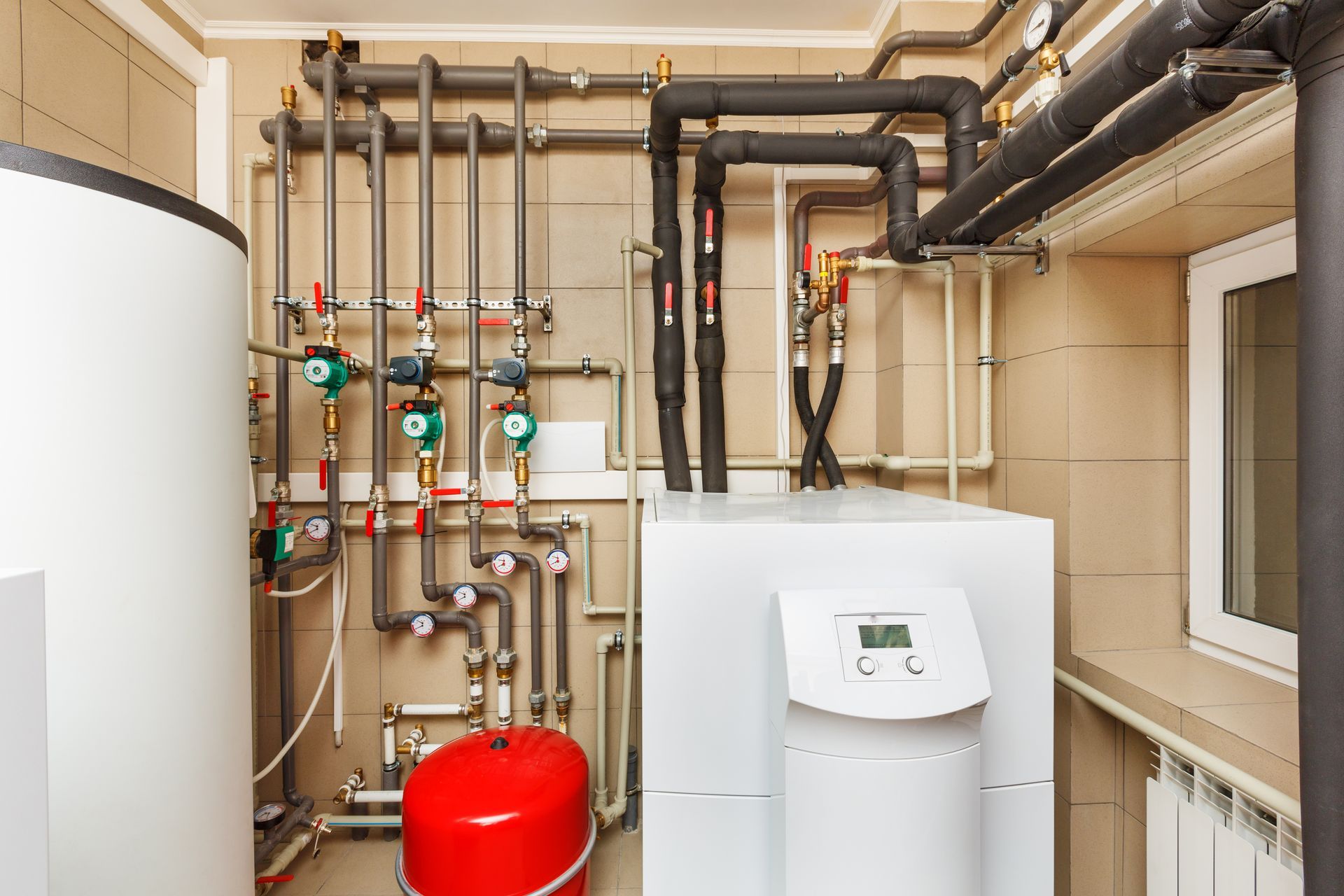 Interior of a utility room with a hot water tank, boiler, and pipes. Gray and black pipes against a tan wall.