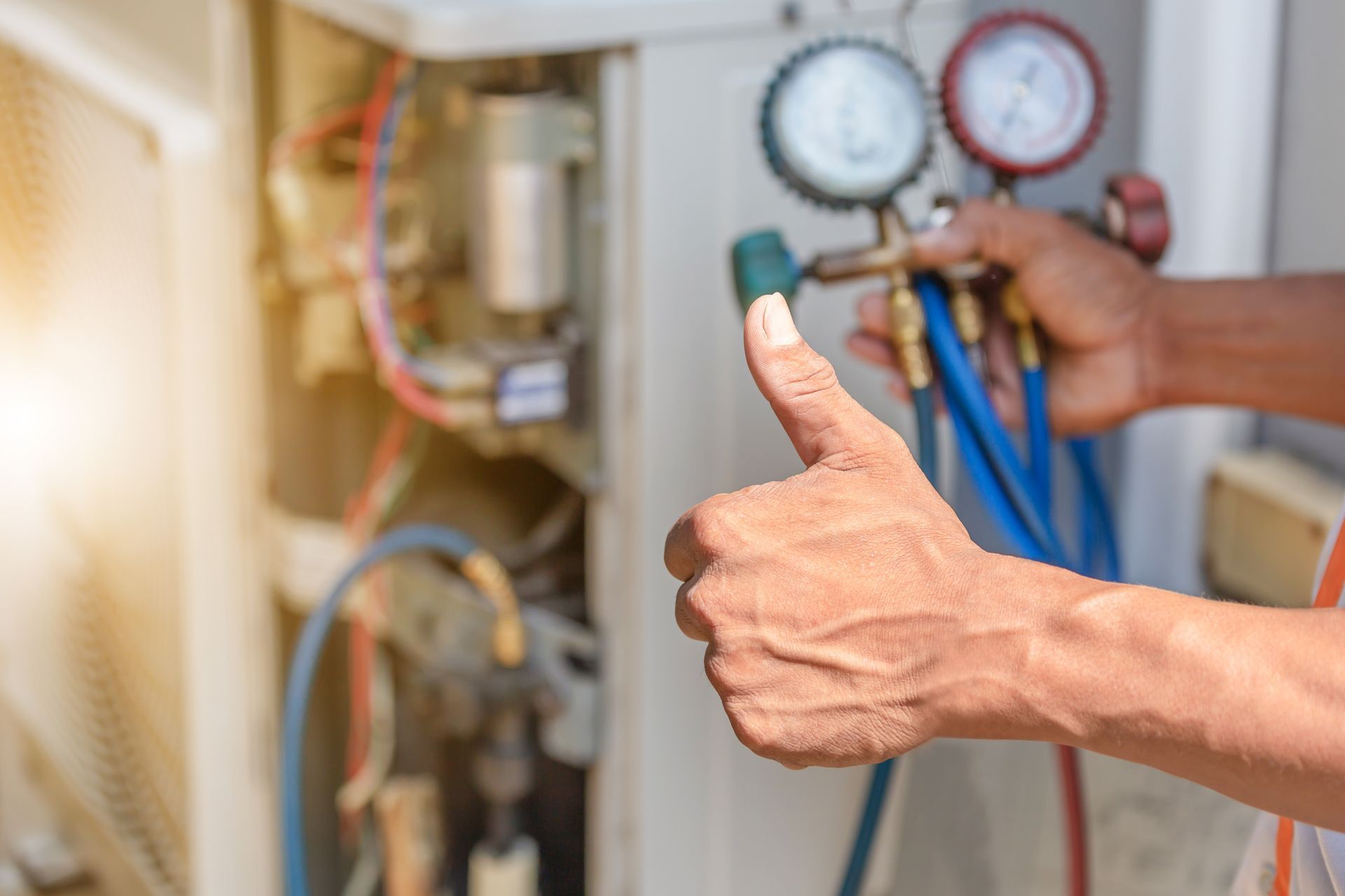 HVAC technician giving a thumbs up while holding gauges, next to AC unit.