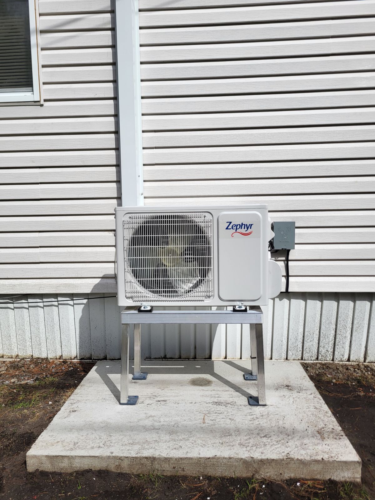 Un climatiseur blanc est posé sur une plate-forme en béton devant une maison blanche.