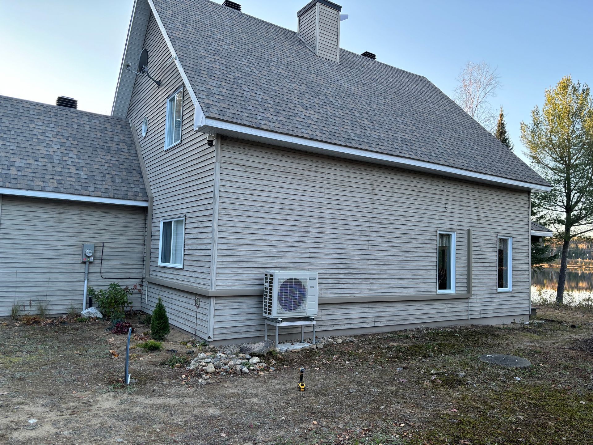 Une maison blanche avec un toit gris et un petit climatiseur sur le côté.