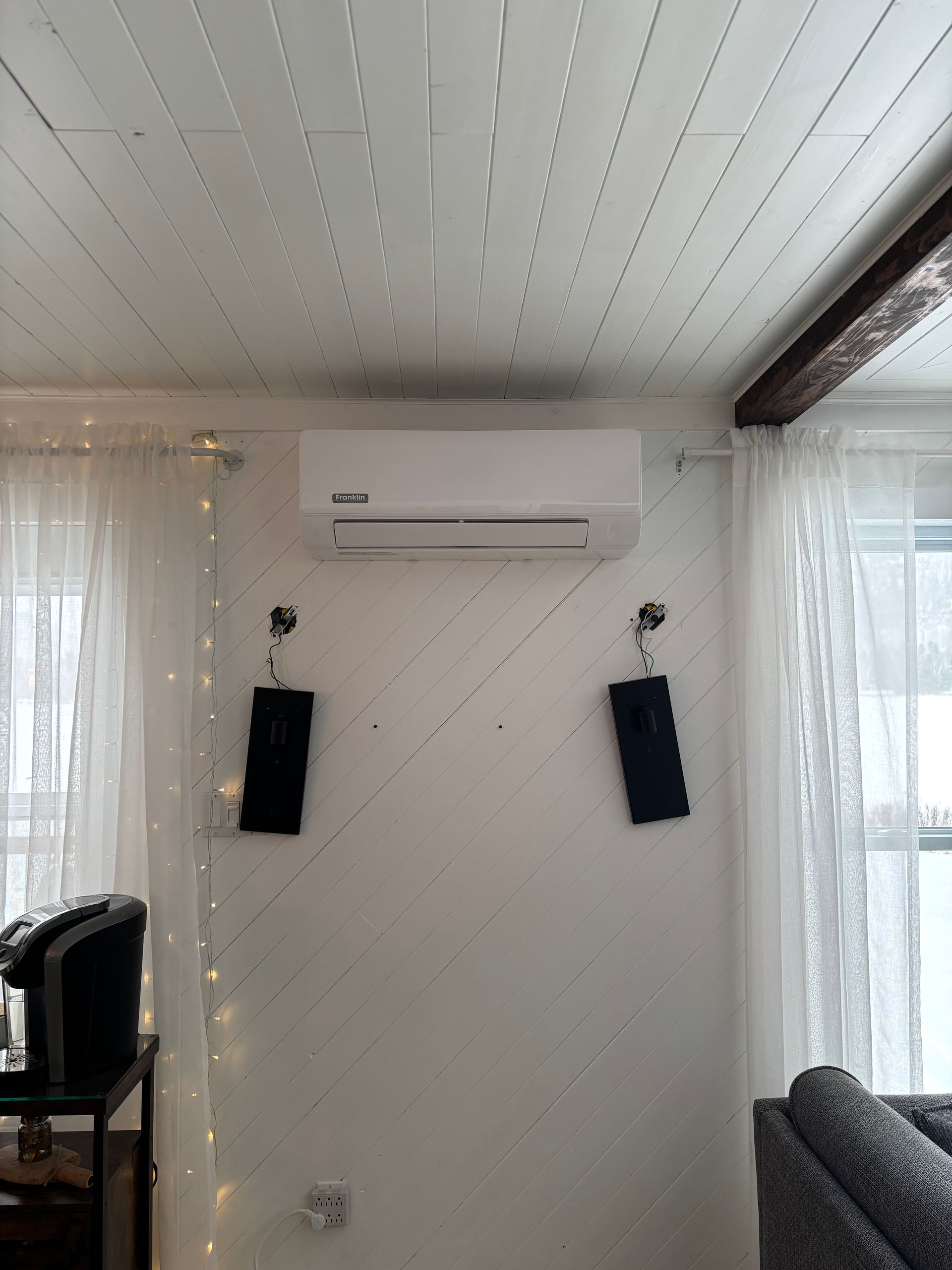 Un salon avec un ventilateur de plafond et des enceintes au mur.