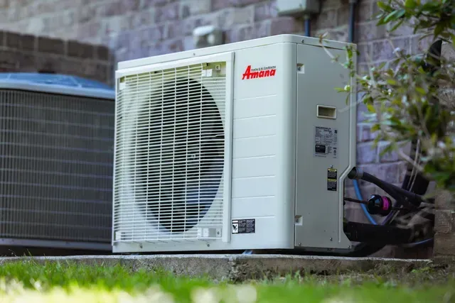 Un climatiseur blanc est posé sur le côté d'un bâtiment en briques.