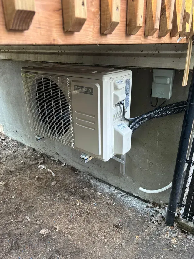 Un climatiseur blanc est posé sur le sol à côté d'un panneau en bois.