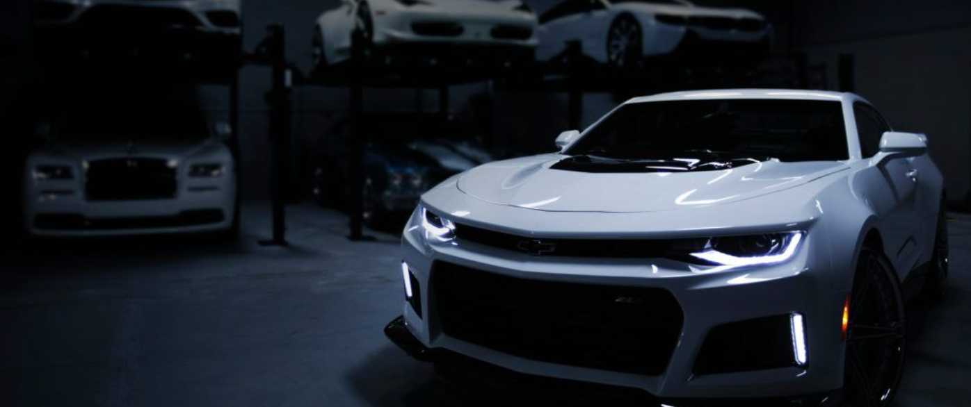 White Chevrolet Camaro in a dimly lit garage, surrounded by other cars.