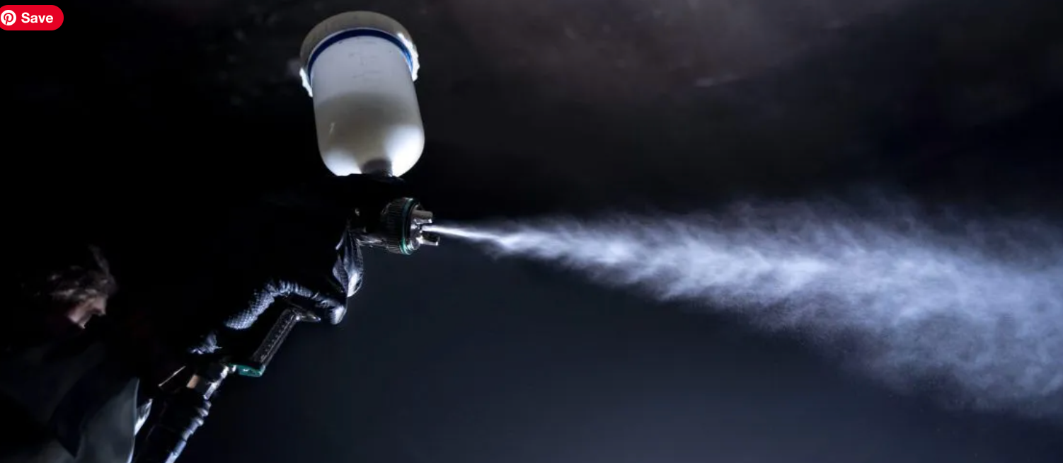 A person spraying a mist with a paint gun in a dark environment.