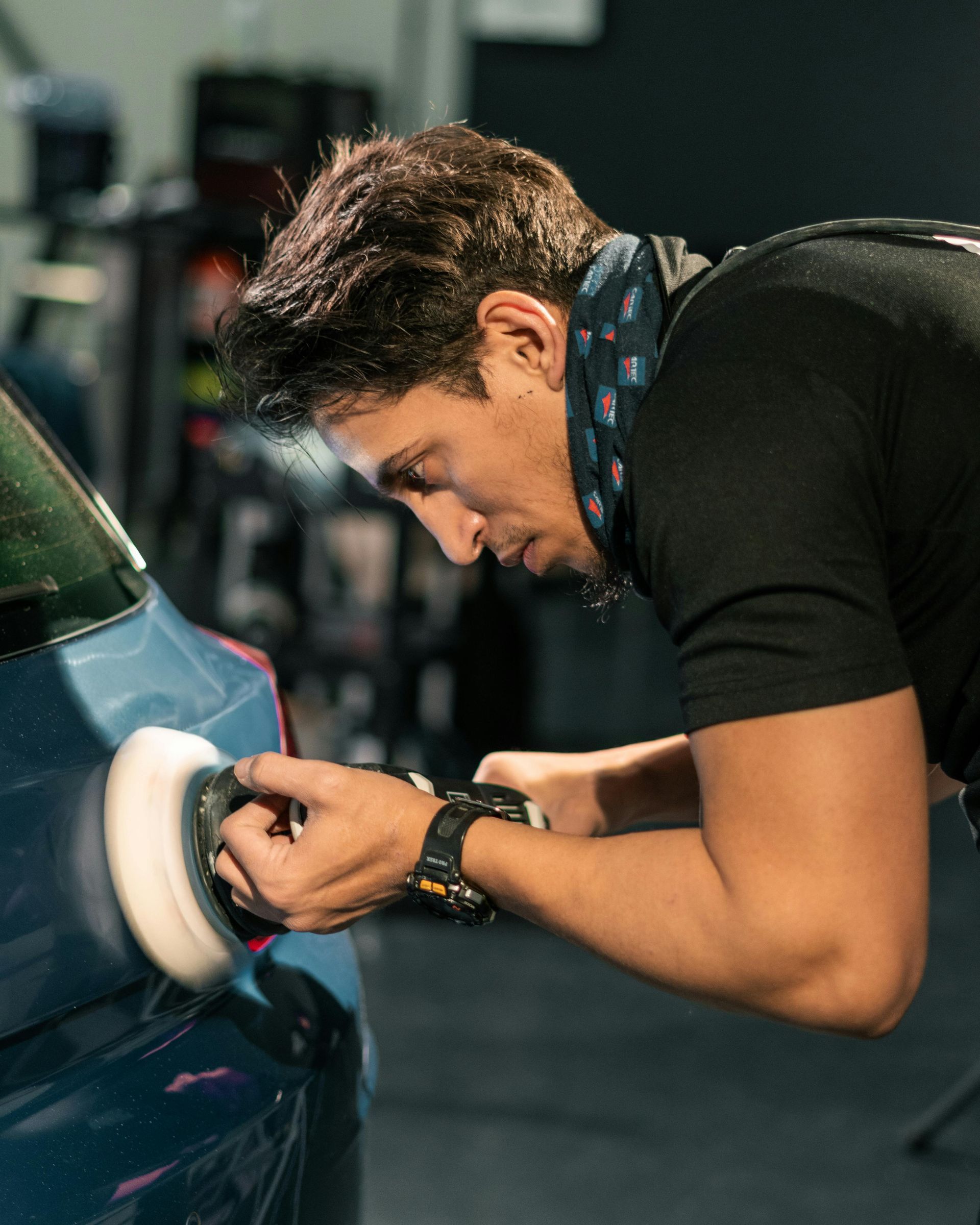 Man polishing a blue car with a buffer in a shop.