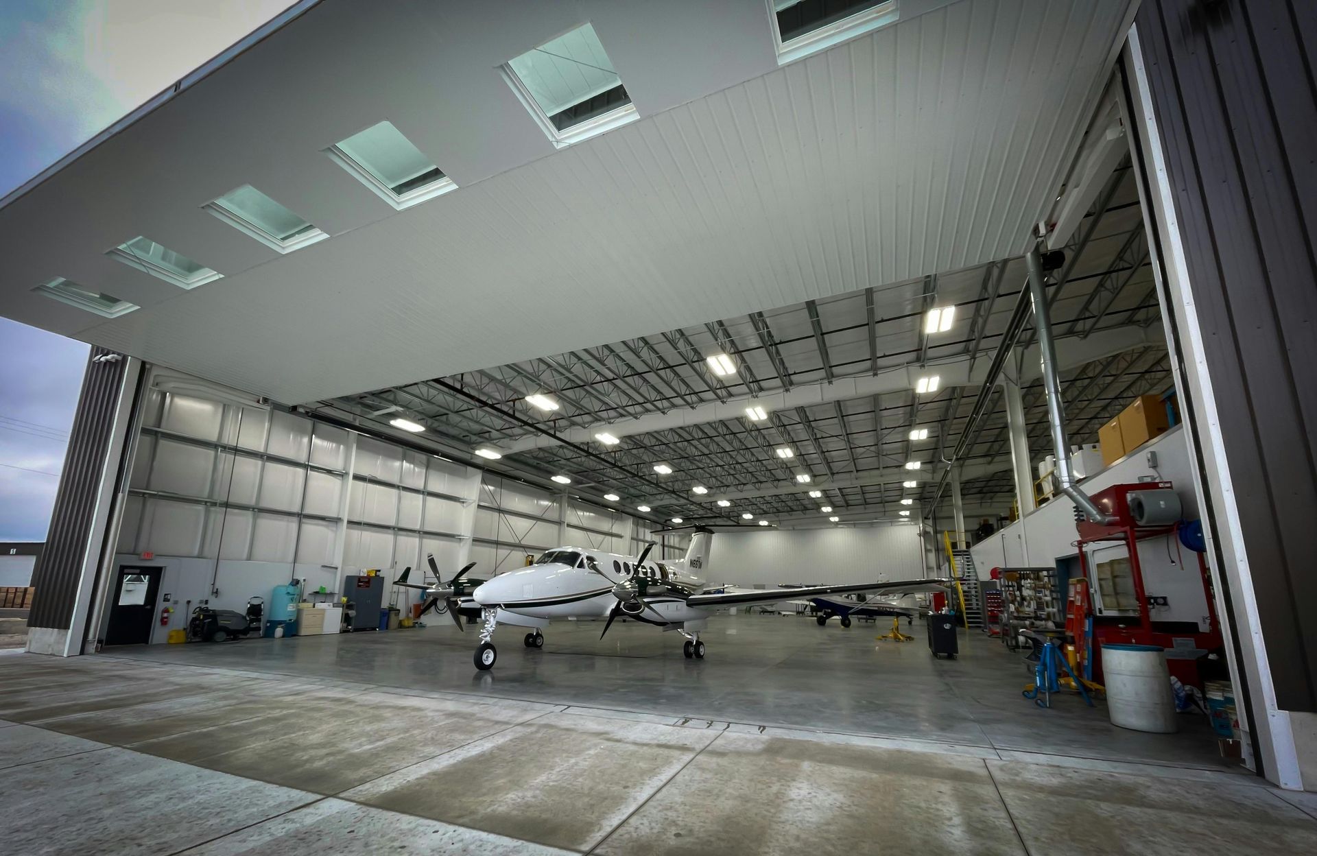Airplane inside a hangar with an open door. The hangar is brightly lit with overhead lights.