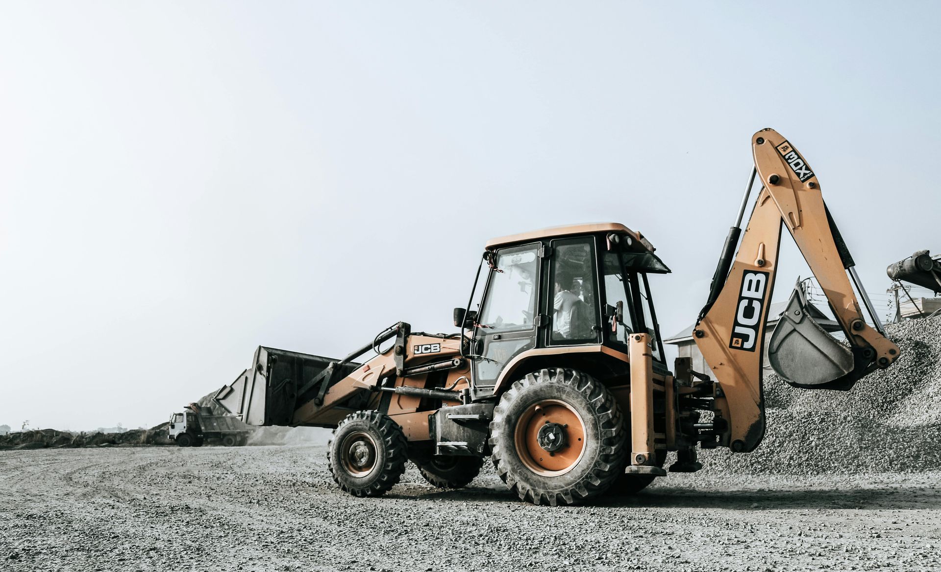 Yellow and gray JCB backhoe loader on a gravel surface.