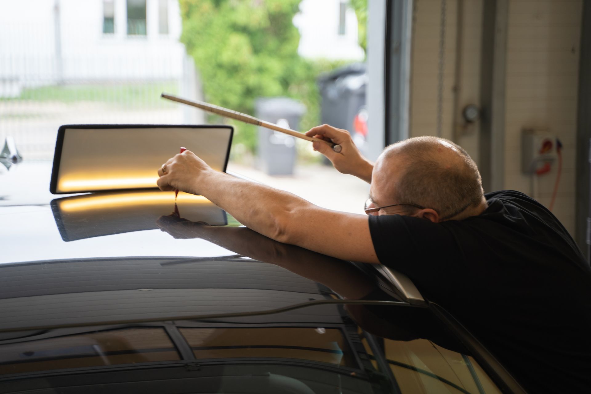 Man using tools to remove a dent from a car's roof in a garage.