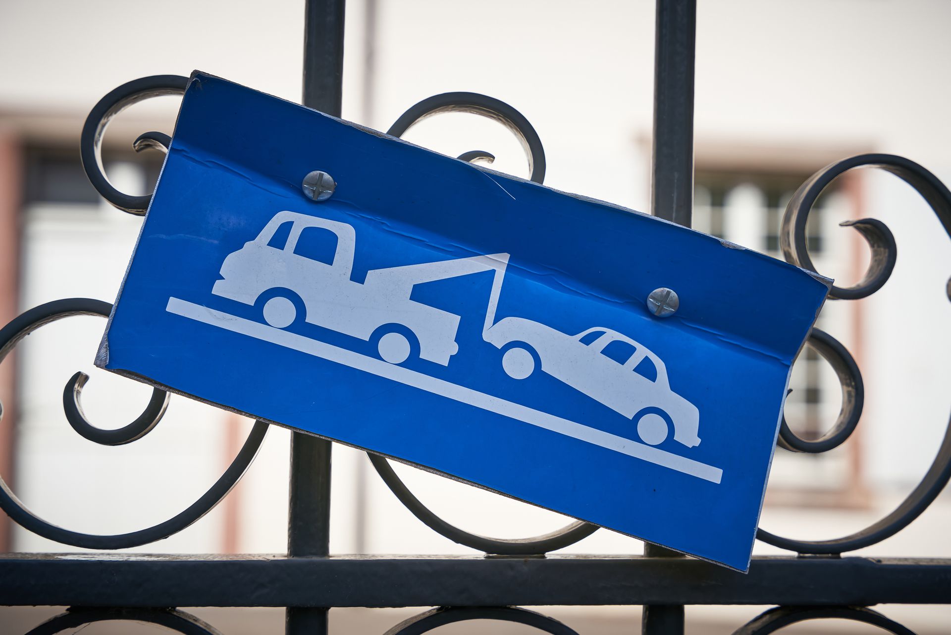 Blue sign with a tow truck towing a car, attached to a black wrought iron gate.