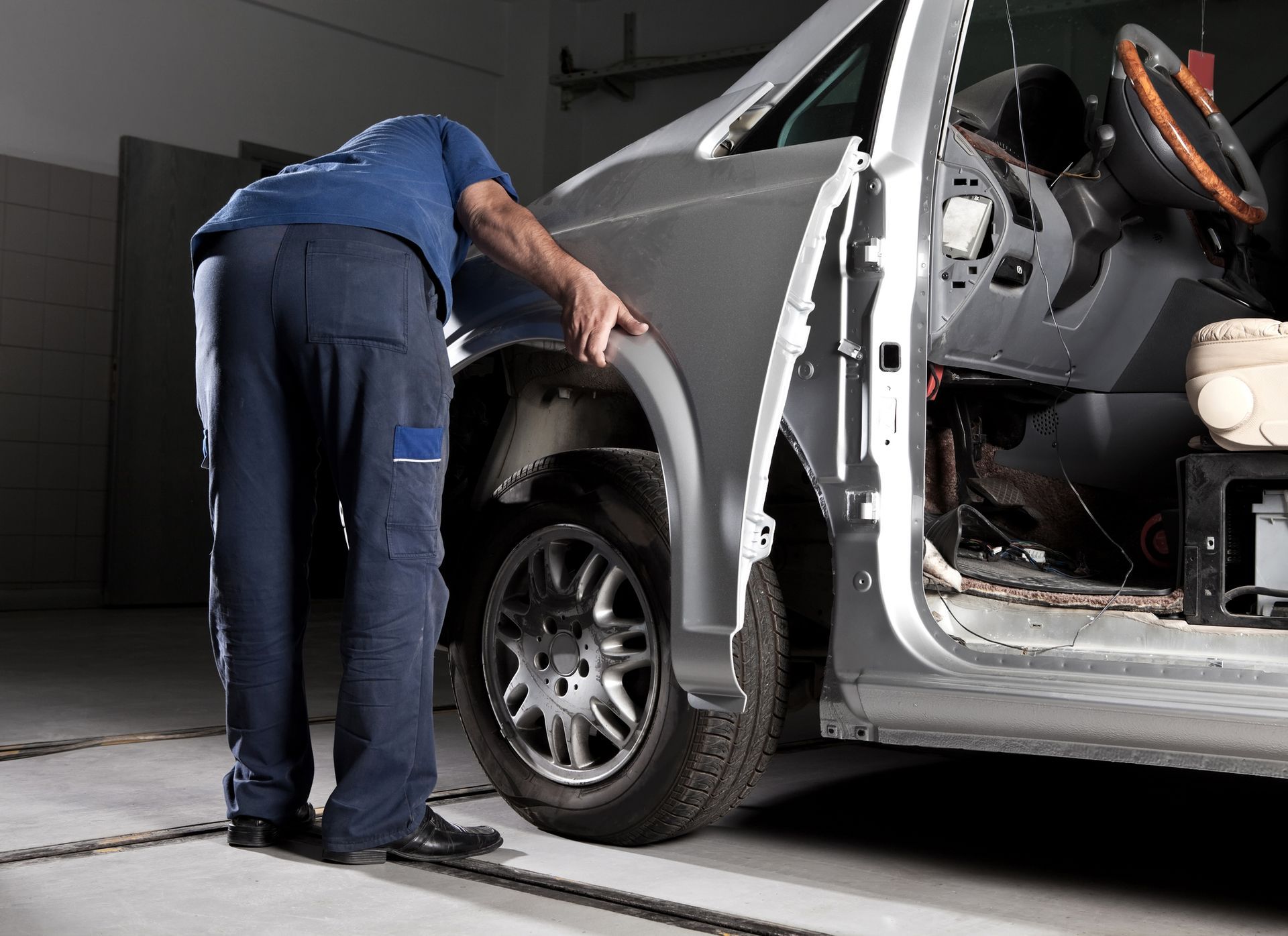 Mechanic inspecting a silver car's front fender in a garage.