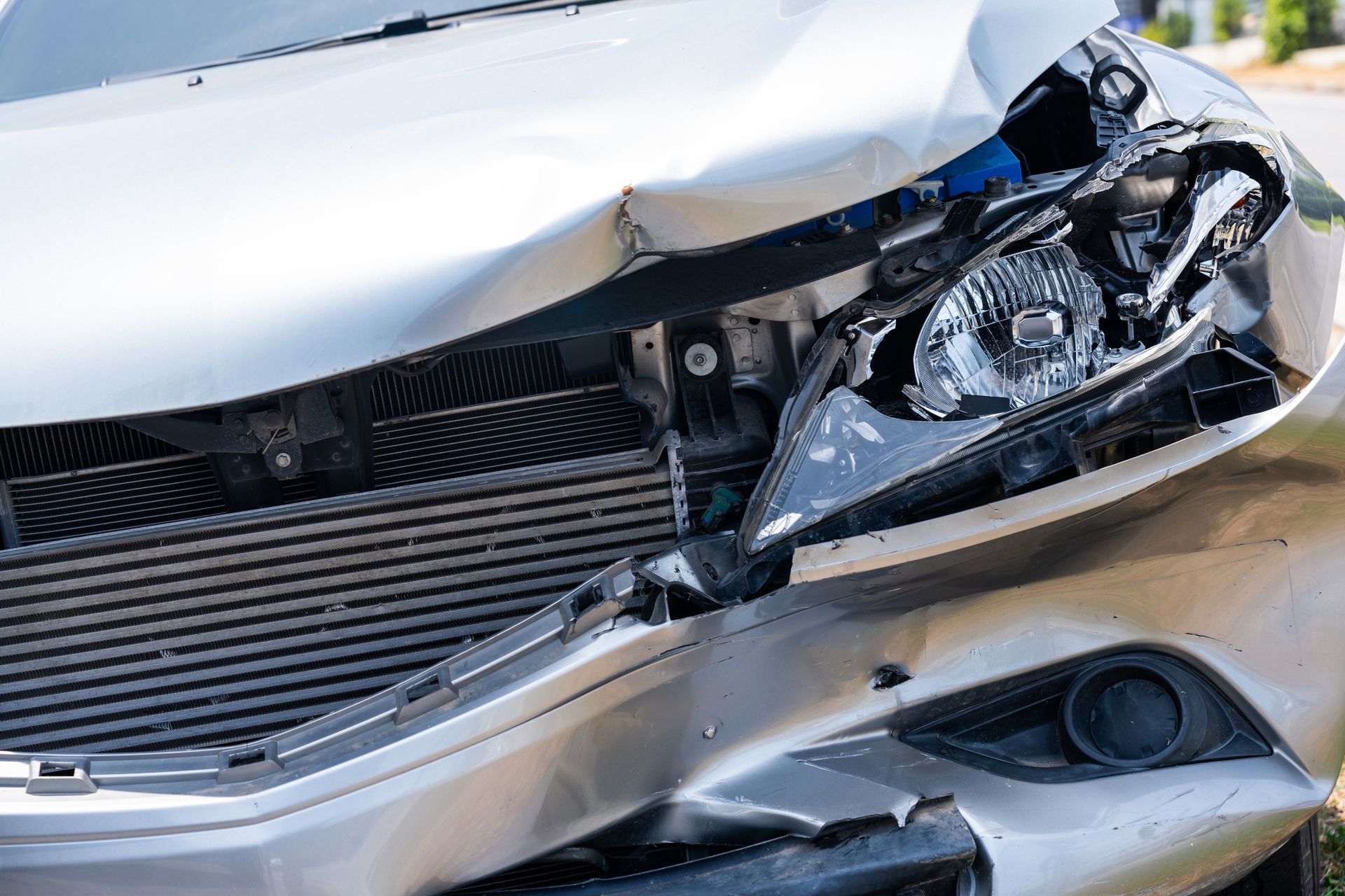 Damaged silver car front; crumpled hood and broken headlight after a collision.