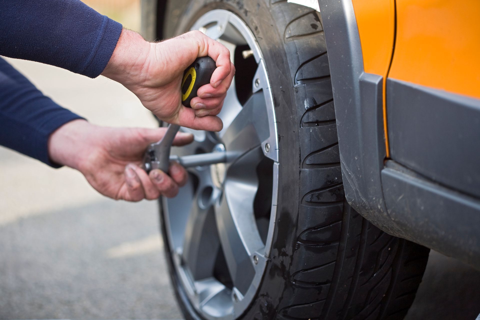 Person using a wrench to loosen lug nuts on a car tire.