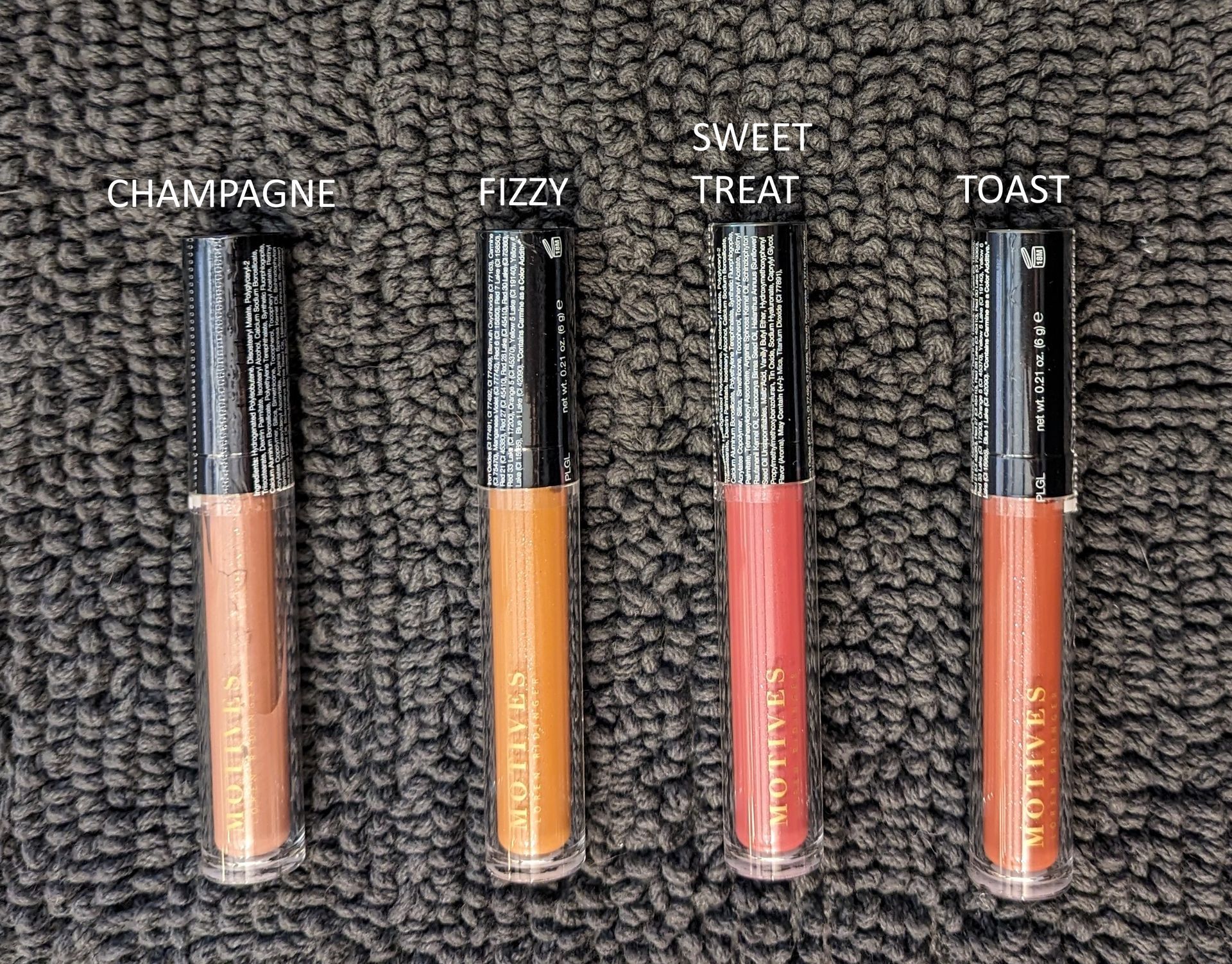 Four bottles of liquid lipstick are lined up on a carpet.