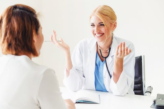 Doctor smiling, gesturing while speaking to a patient at a desk.