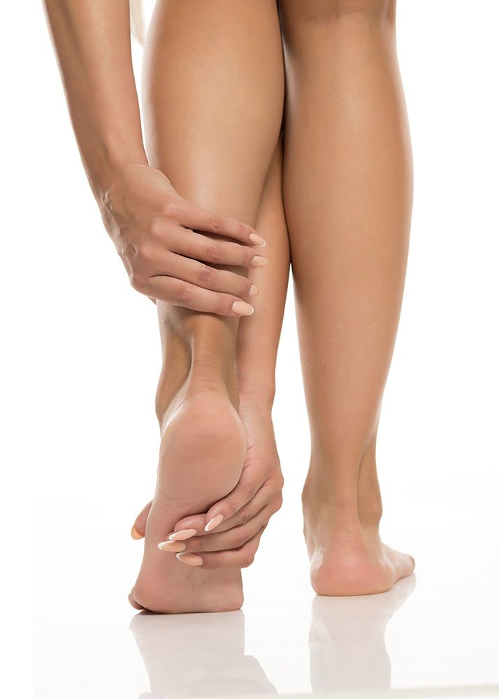 Woman holding her right ankle and foot, possibly in pain, against white background.
