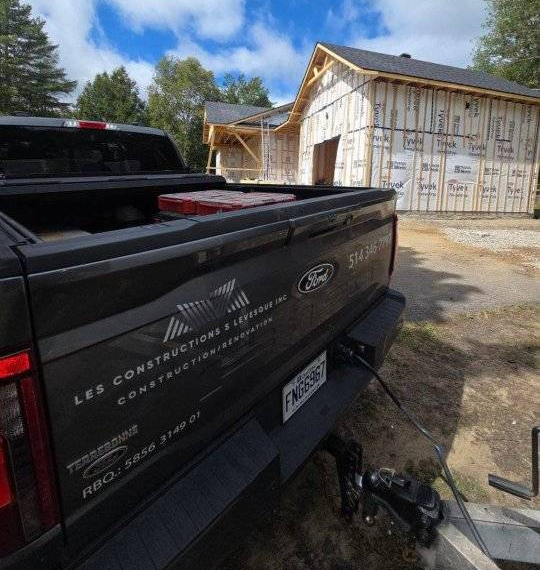Un camion Ford gris foncé sur un chantier de construction, avec une maison en construction à l'arrière-plan.