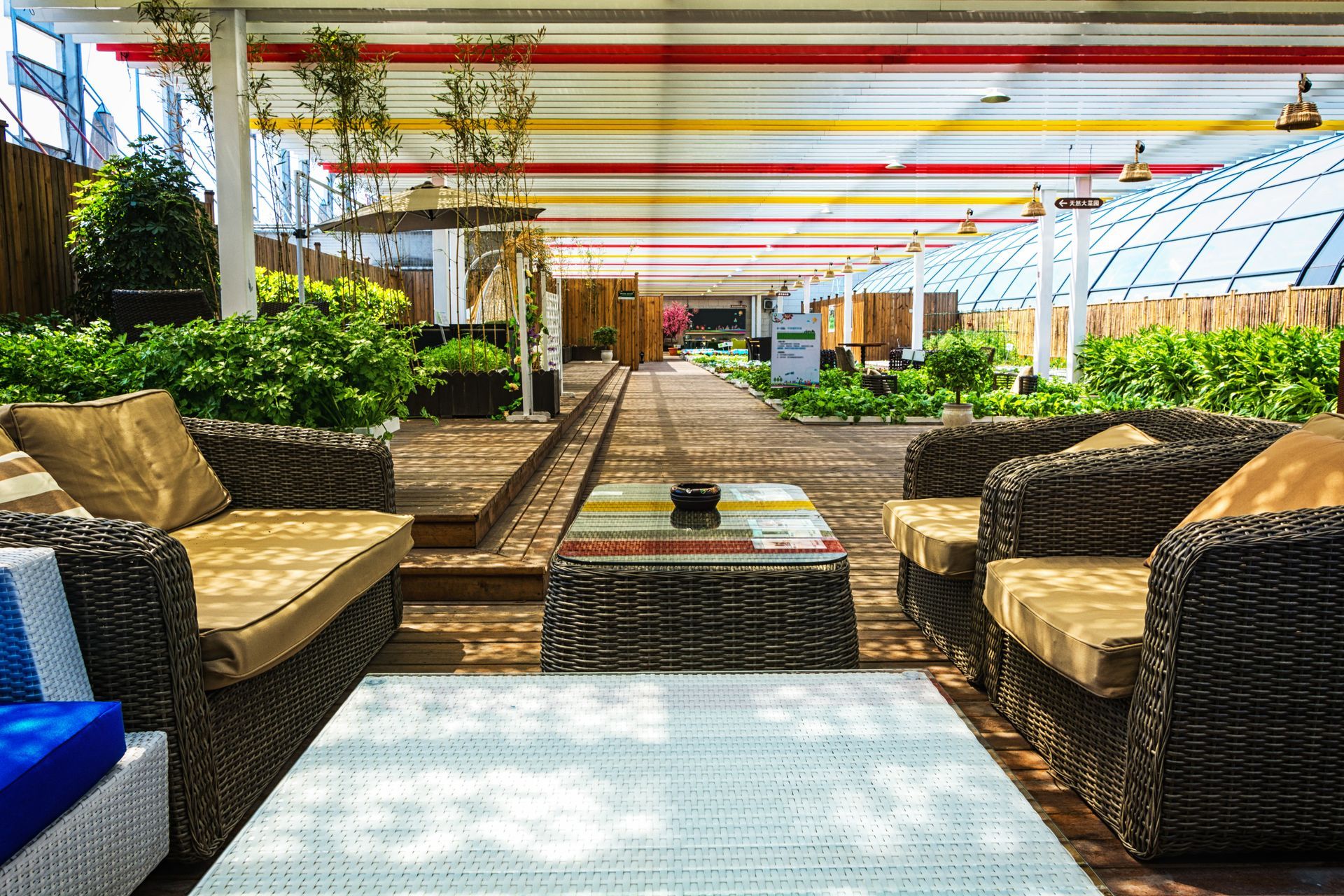 Espace lounge extérieur avec mobilier en osier, plantes et un auvent à rayures colorées.