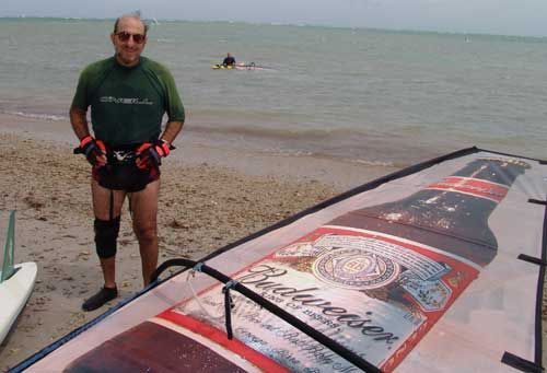A man standing next to a budweiser sail on the beach