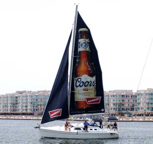 A sailboat with a large coors bottle on the sail