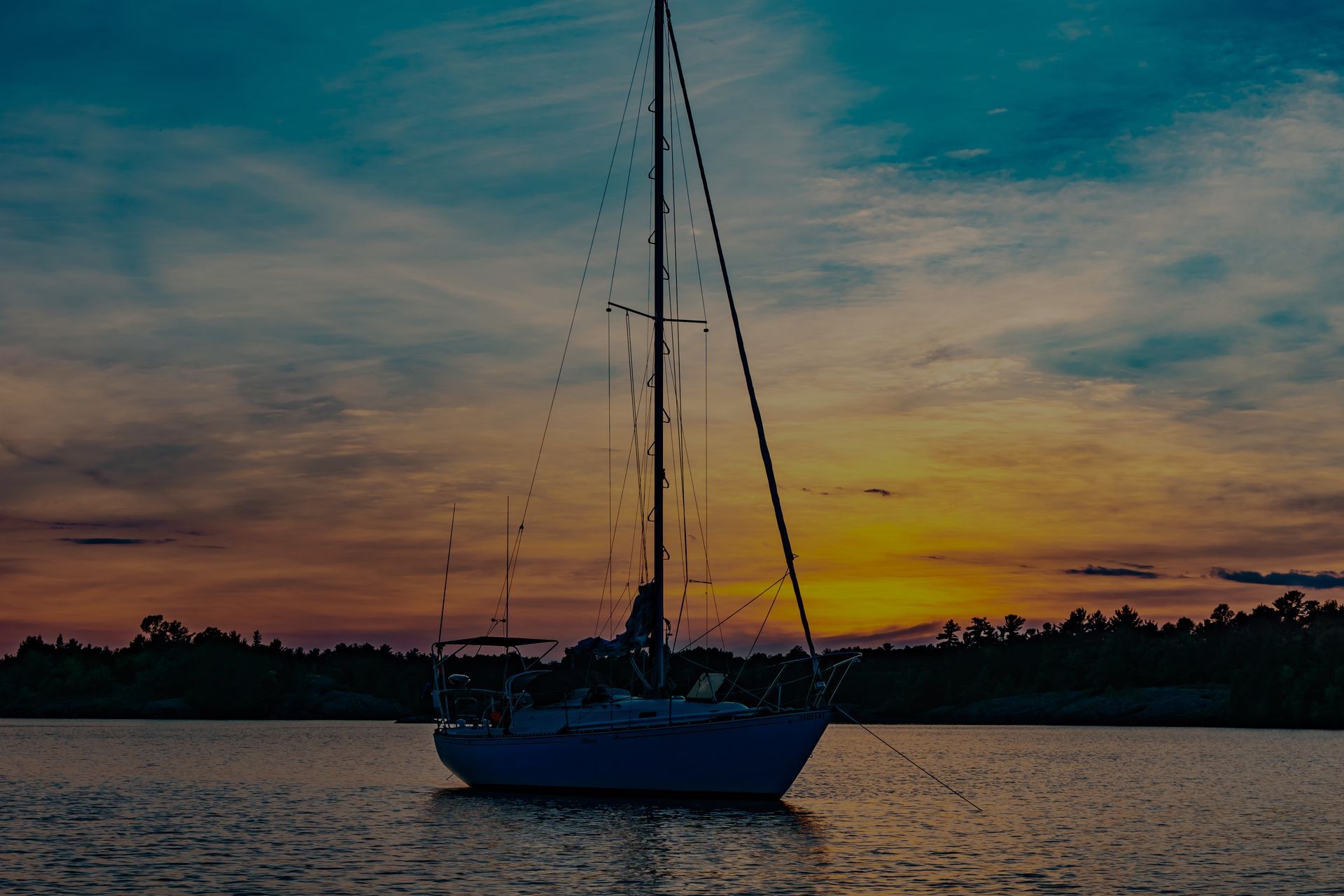 A sailboat is floating on top of a body of water at sunset.