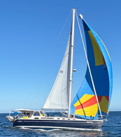 A sailboat with a colorful blue, yellow, and orange spinnaker sailing on blue water under a clear sky.