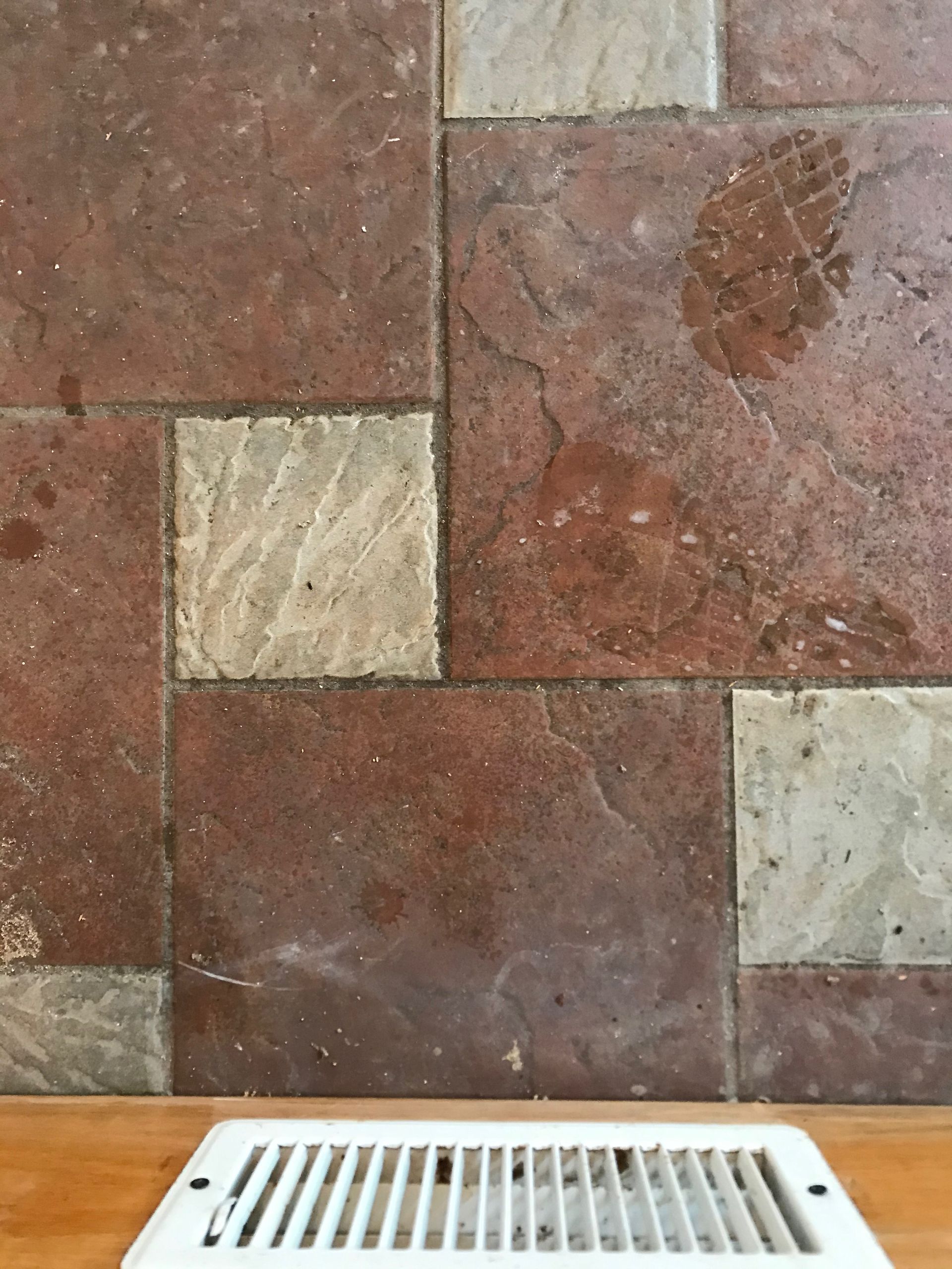 A white vent on a wooden floor next to a tiled wall