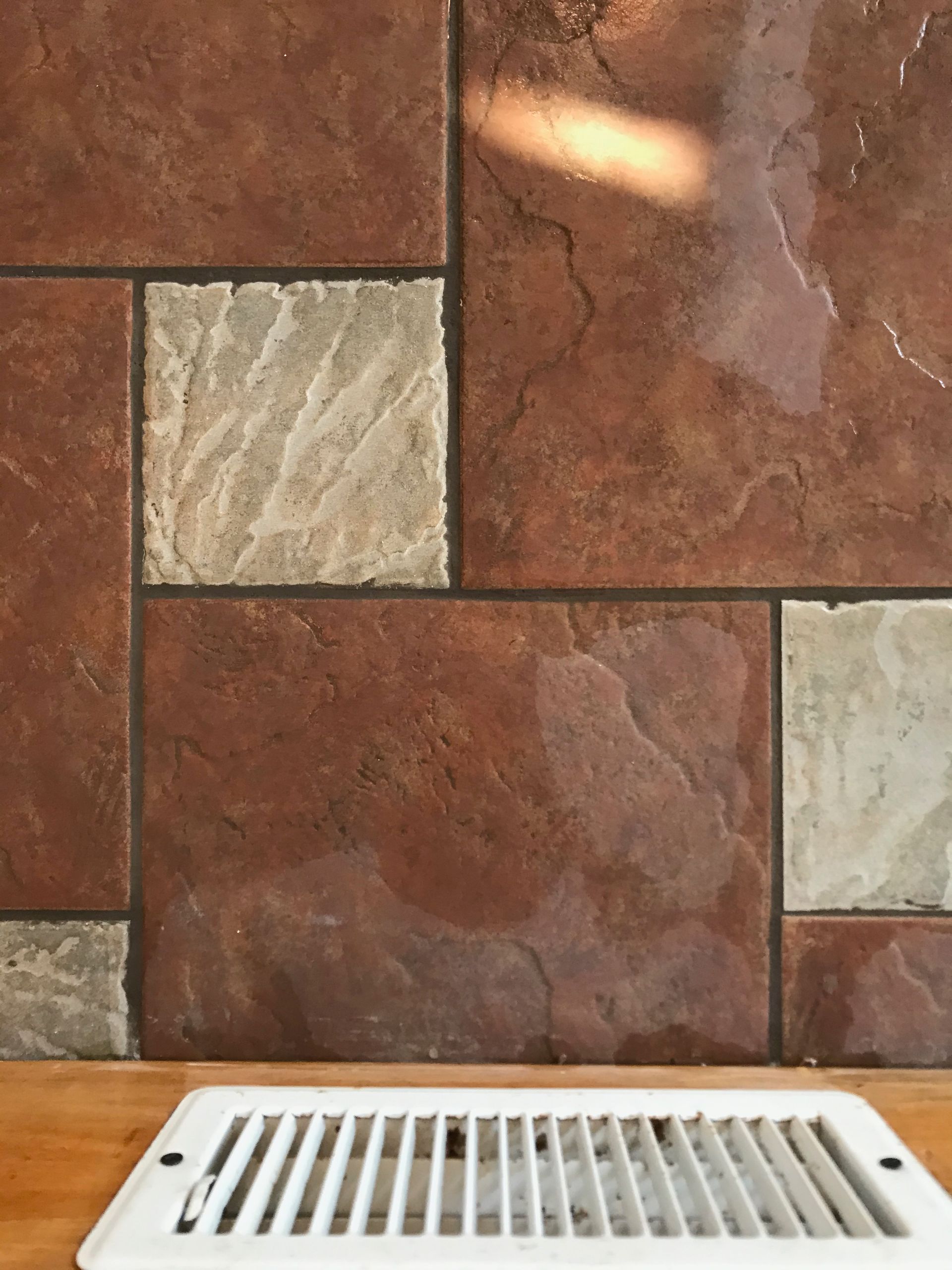 A brown tiled wall with a white vent on the floor