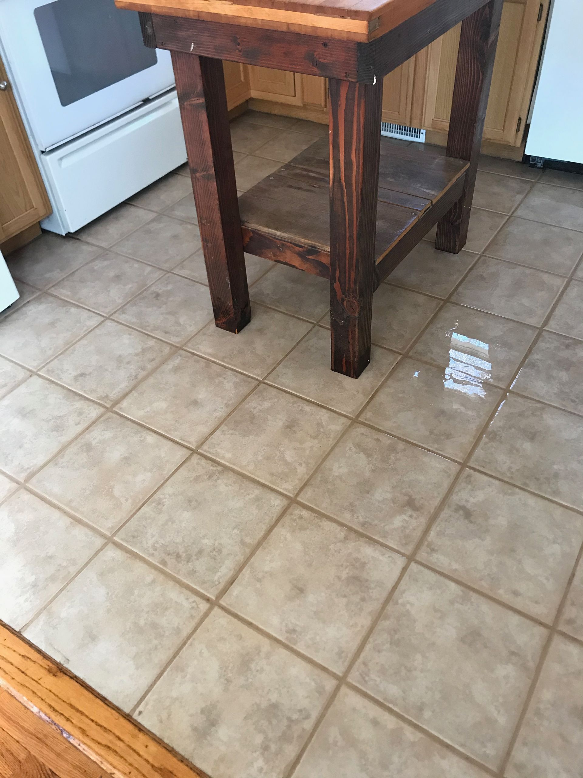 A wooden table sits on a tiled floor in a kitchen