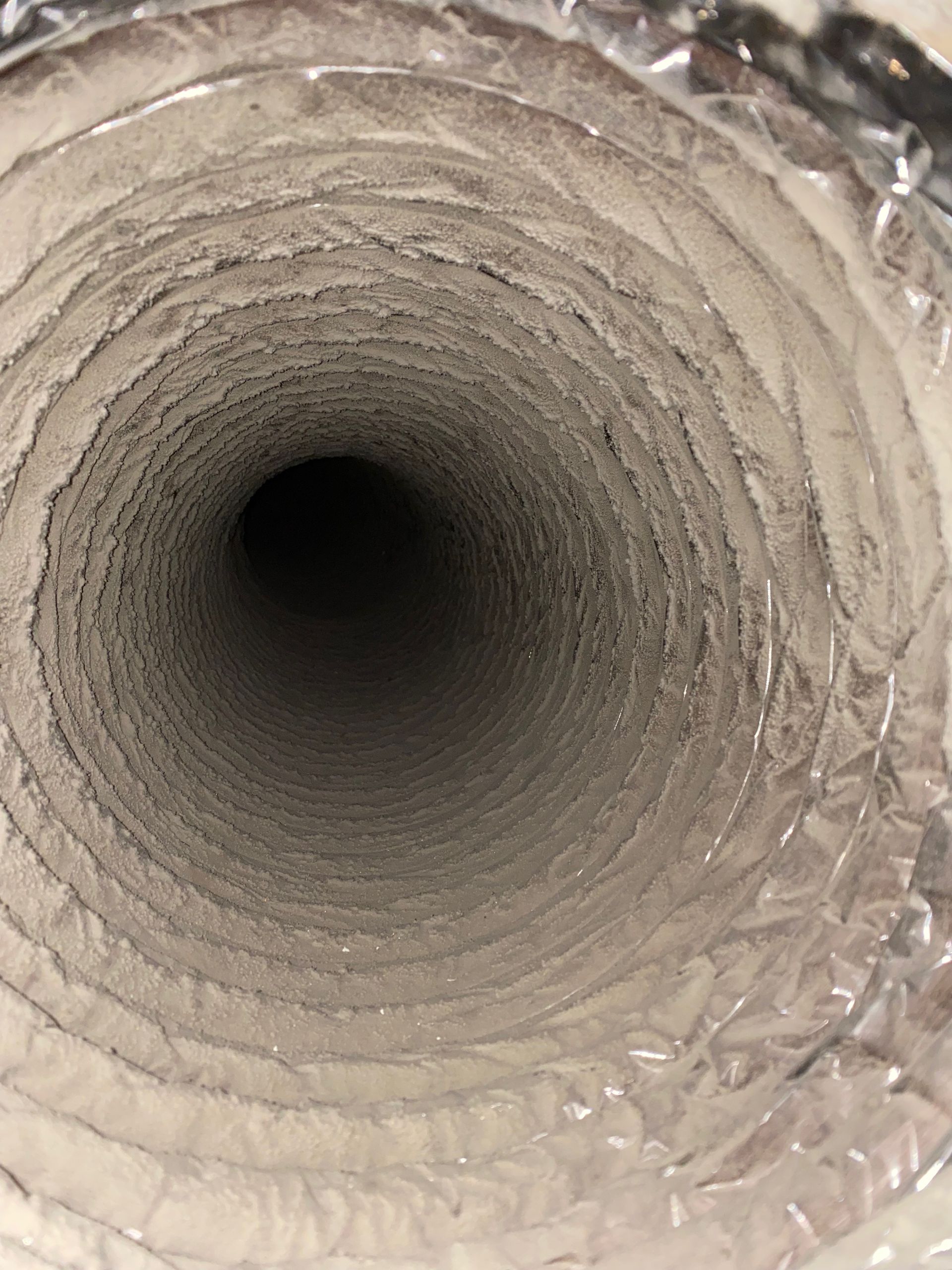 A close up of a dirty air duct with aluminum foil covering it.
