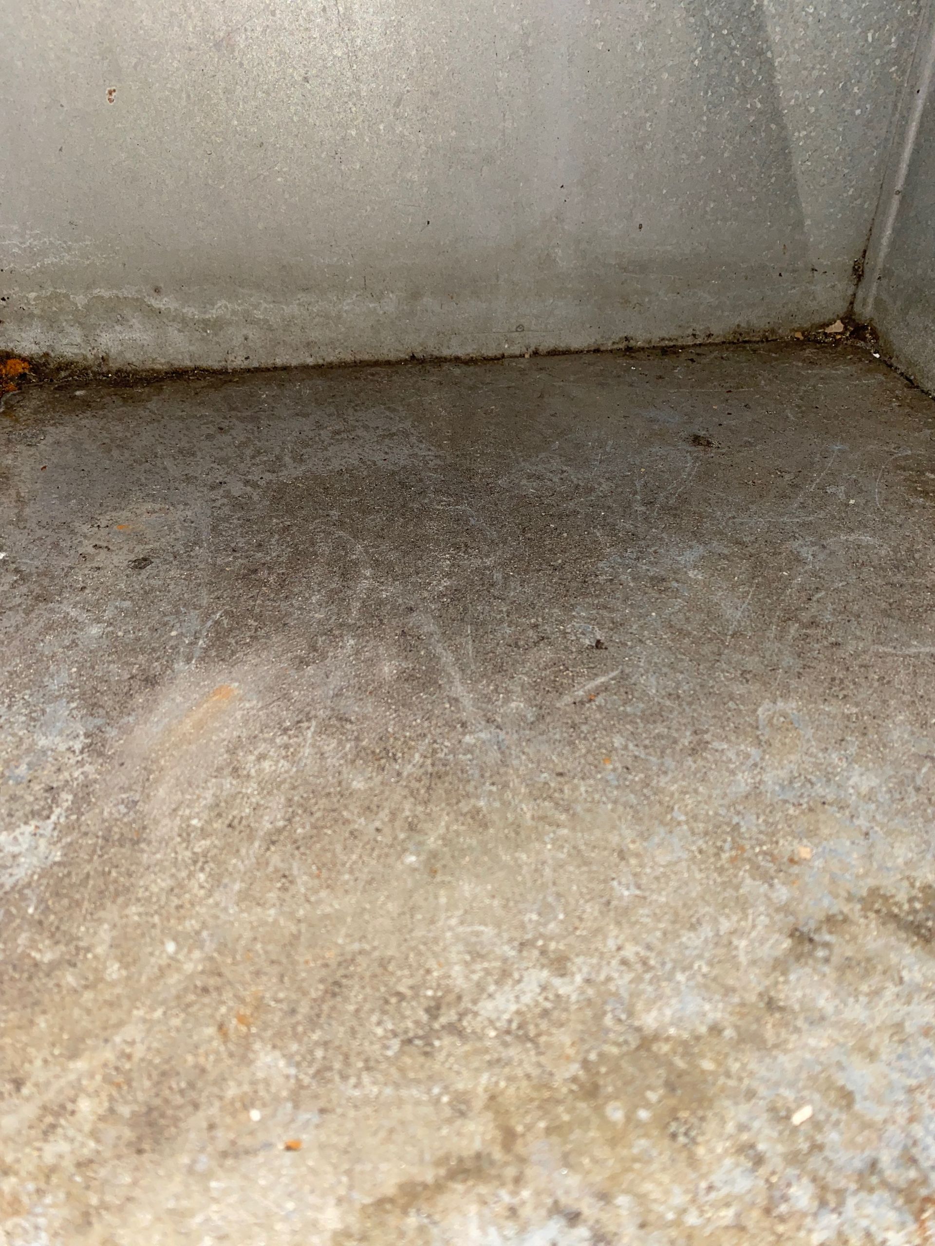 A dirty concrete floor with a white wall in the background