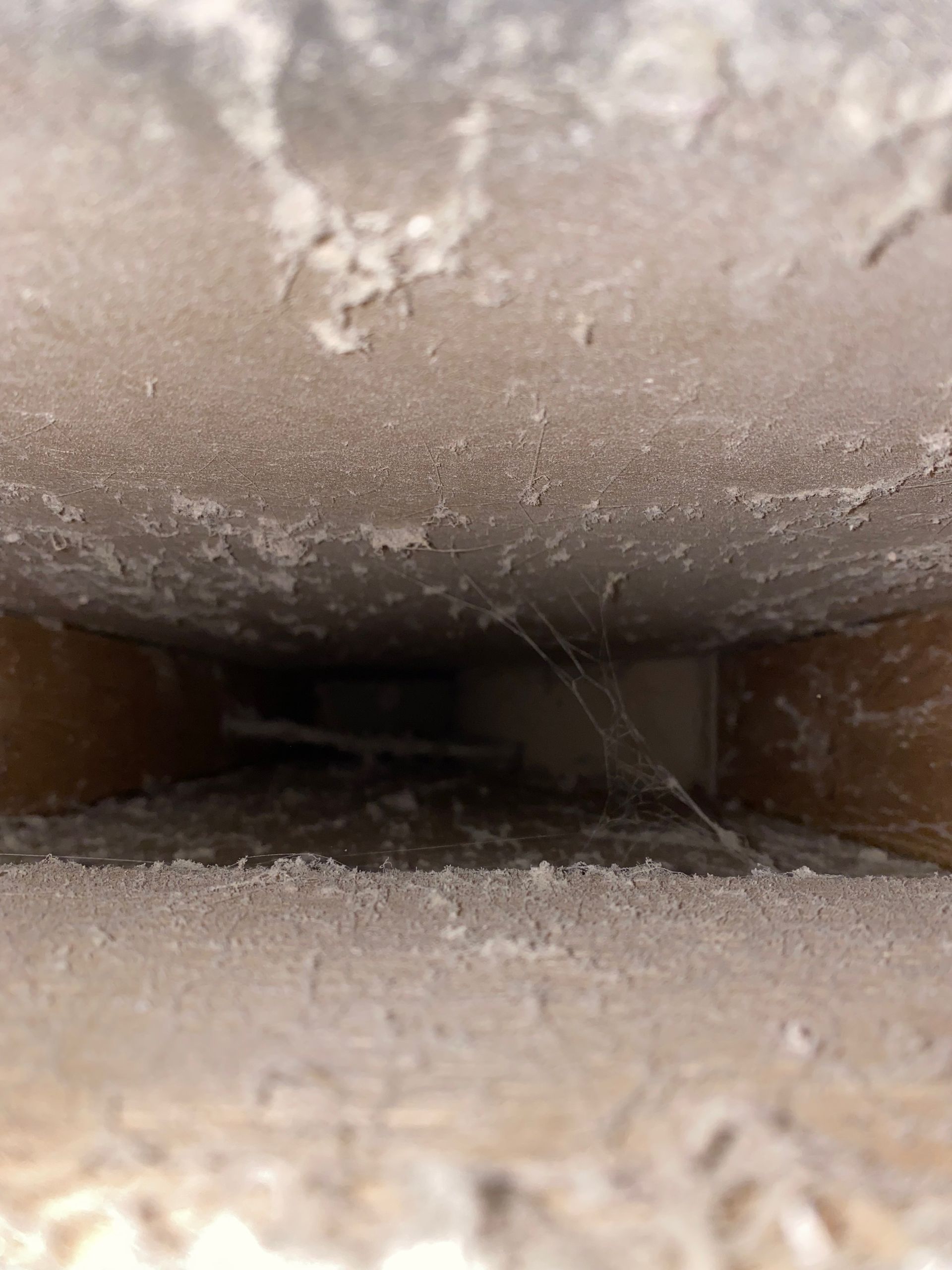A close up of a dirty ceiling with a spider web coming out of it.