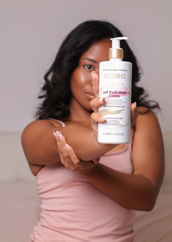 Femme tenant et appliquant une lotion pour le corps, souriante, portant un débardeur rose.